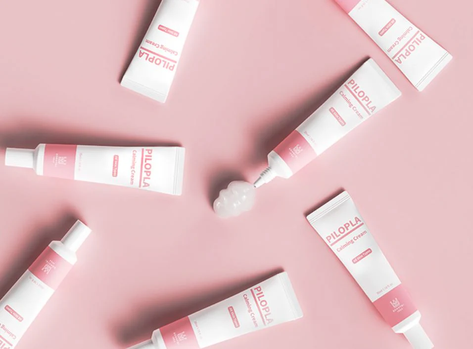 PILOPLA Calming Cream tube arranged aesthetically on a pink background, showcasing its gentle formula for all skin types, especially sensitive skin.