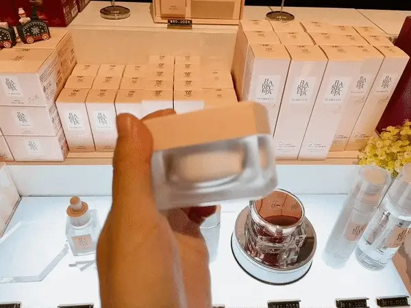 Hand holding BONNY & J Plareceta Cream jar in front of store display with stacked product boxes Hand holding BONNY & J Plareceta Cream jar in front of store display with stacked product boxes